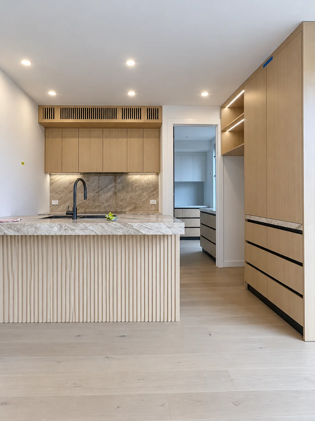 Conrad Residence kitchen with pale timber cabinetry, a fluted island and veined stone worktop in Melbourne.