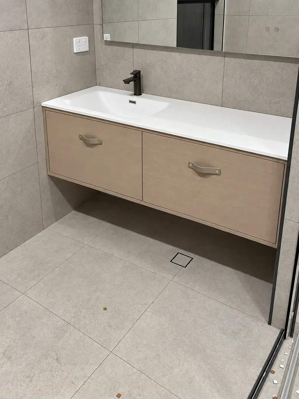 Floating timber vanity with a white single basin, dark tap and two strap handles at the Conrad Residence.